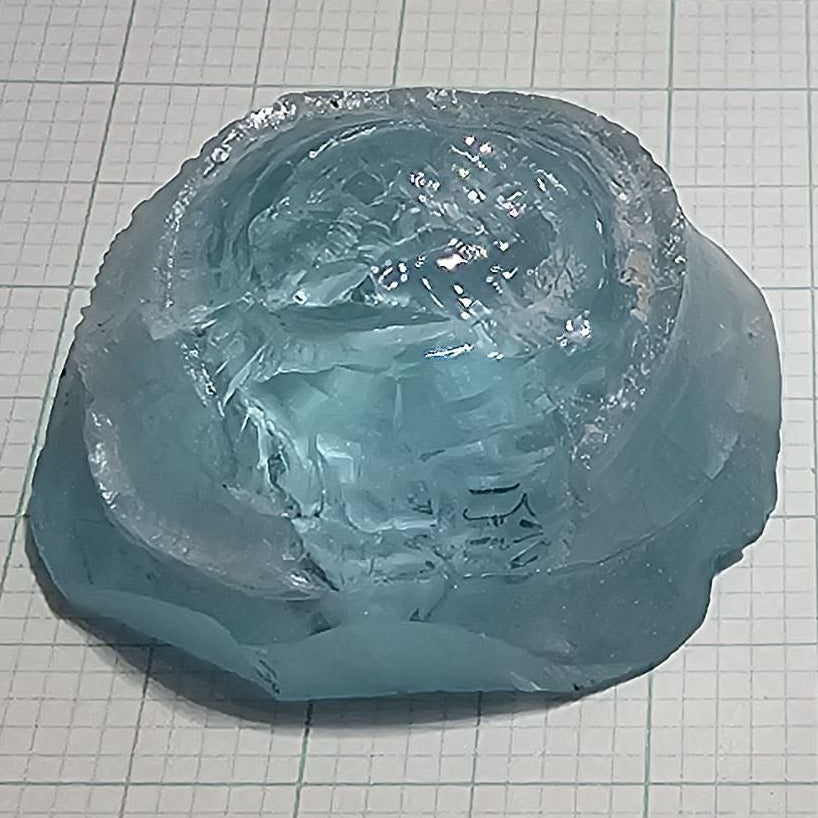Two pieces of light blue laser garnet facet rough, Yb YAG, placed on a checkered background.