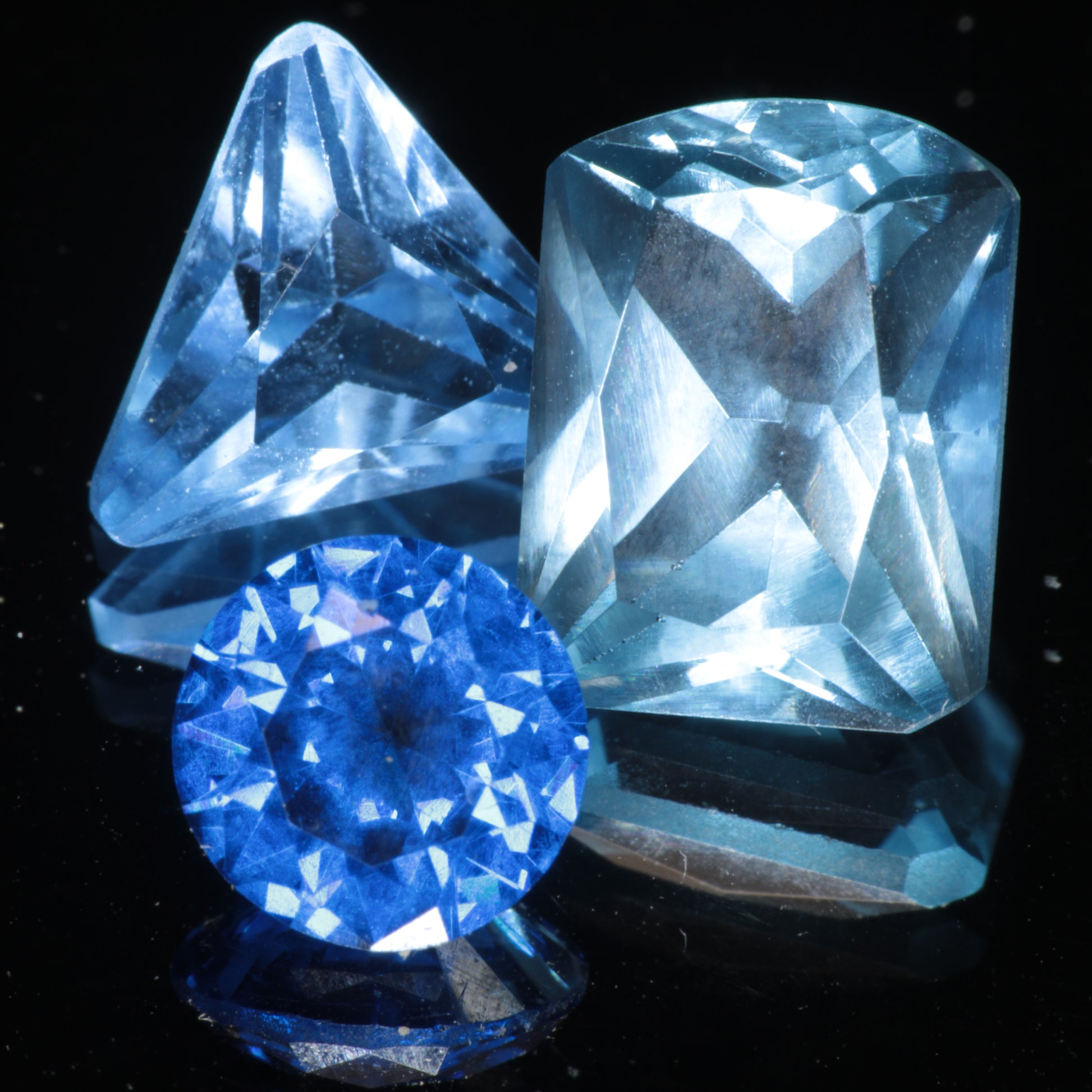Three Blue Spinels of varying color intensity on a black background, faceted labmade spinel gems