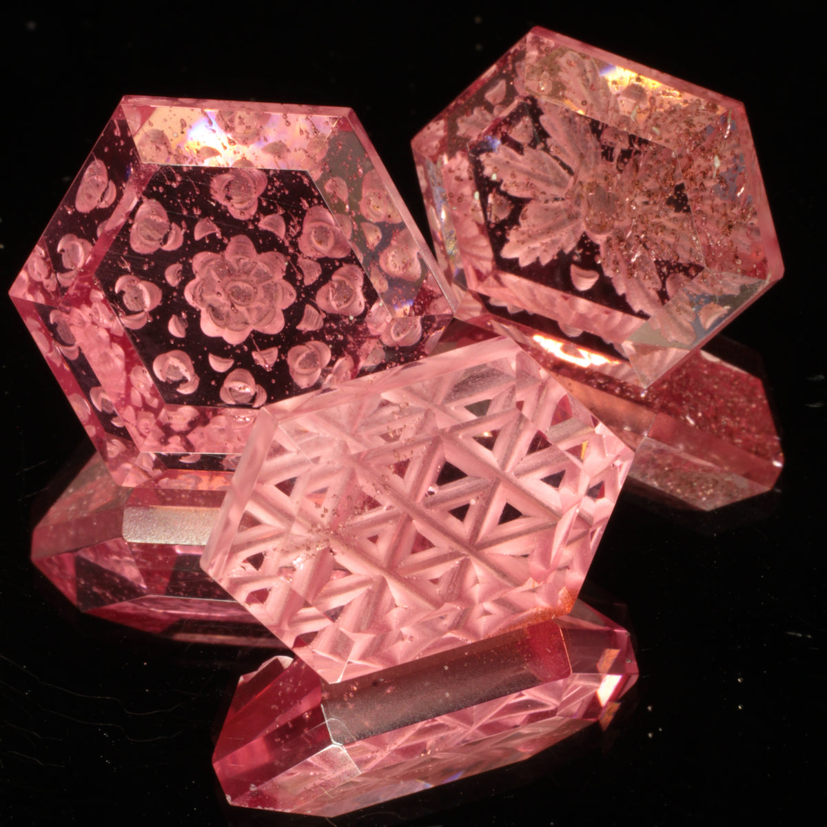 Three Pink Titanium Sapphire Gemstones carved into hexagons on a dark background