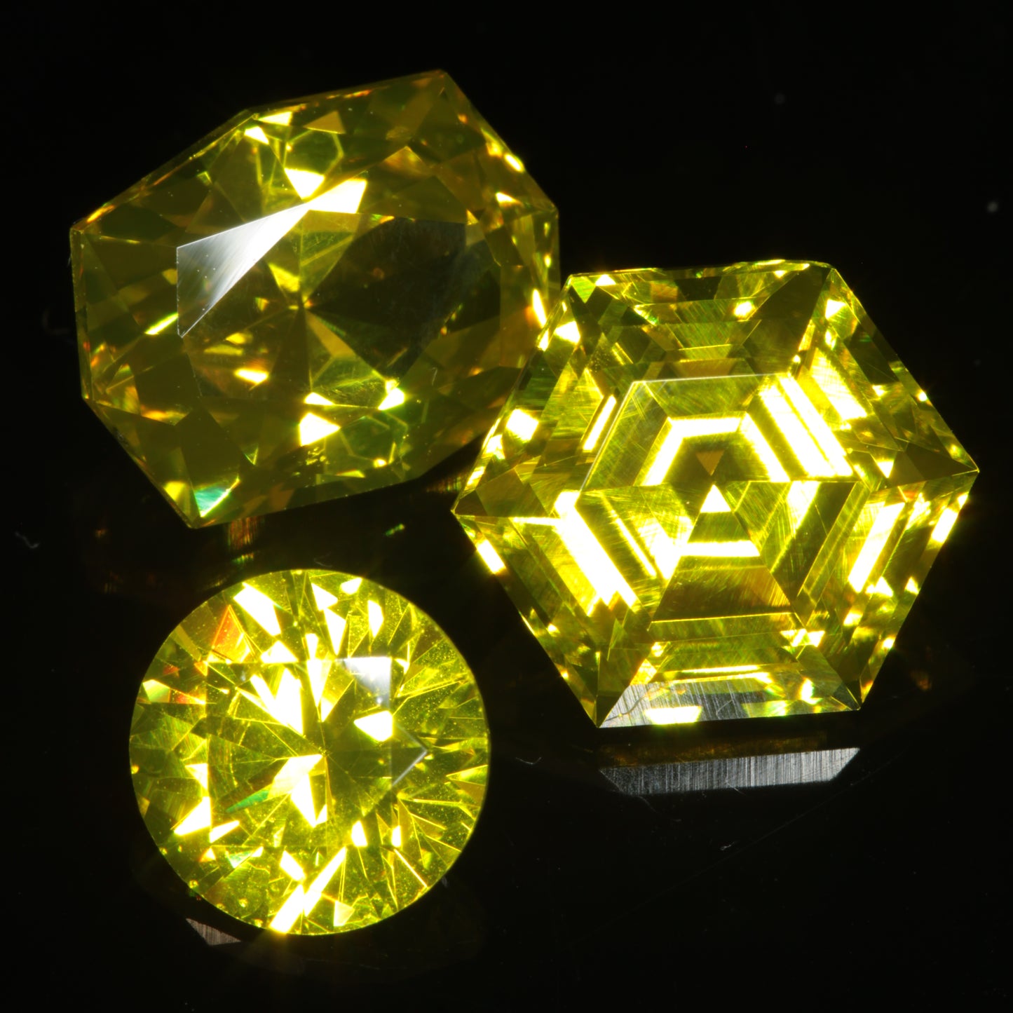 Three bright yellow faceted Ce/Nd YAG gemstones on a dark background