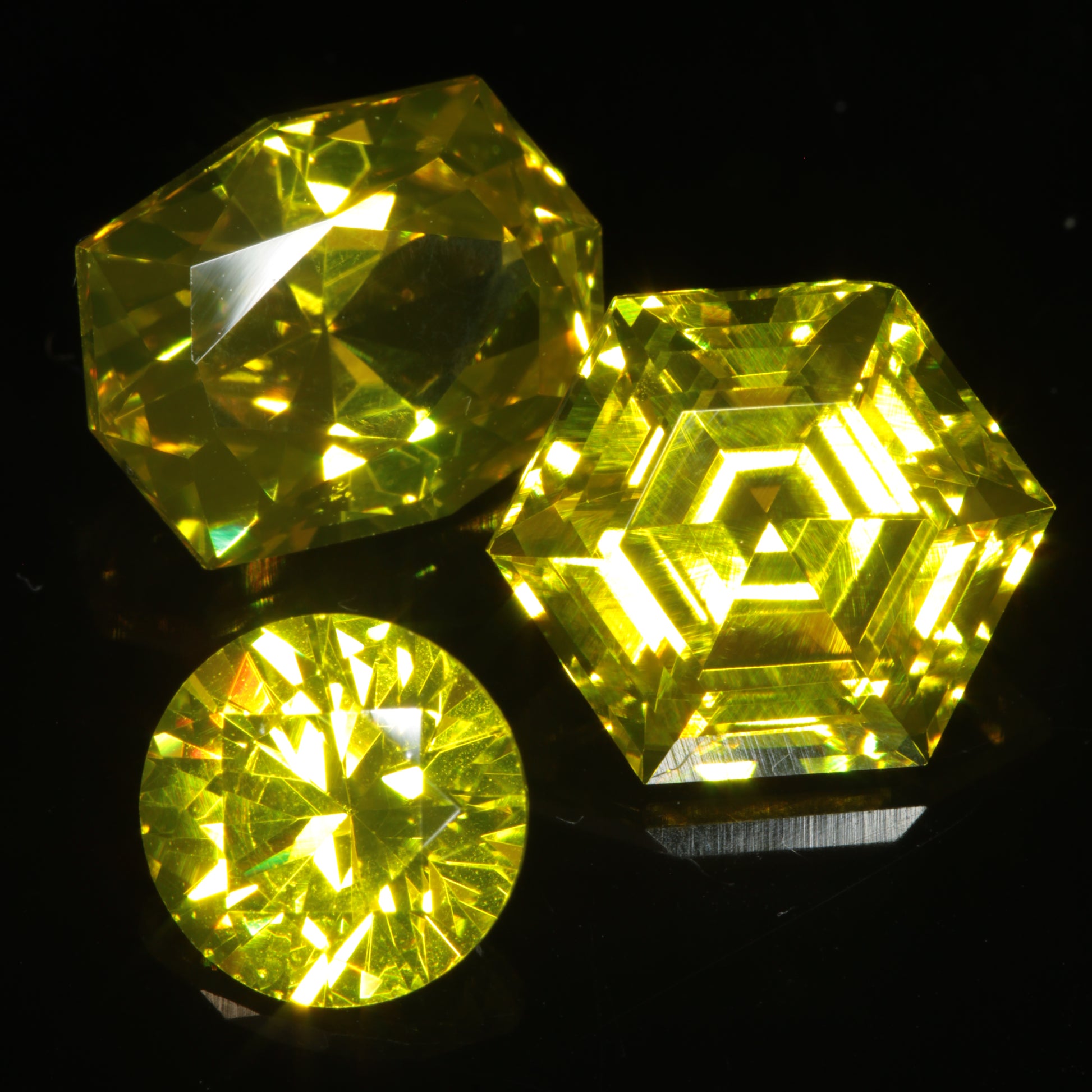 Three bright yellow faceted Ce/Nd YAG gemstones on a dark background