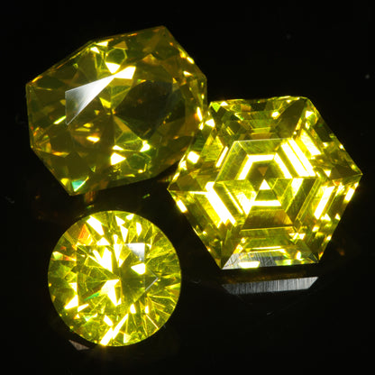 Three bright yellow faceted Ce/Nd YAG gemstones on a dark background