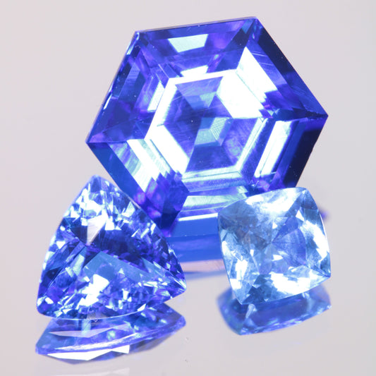 Three vivid blue spinel gemstones, with a large hexagon at the top, a trillion at the bottom left, and a light blue cushion at the bottom right, on a gray background.