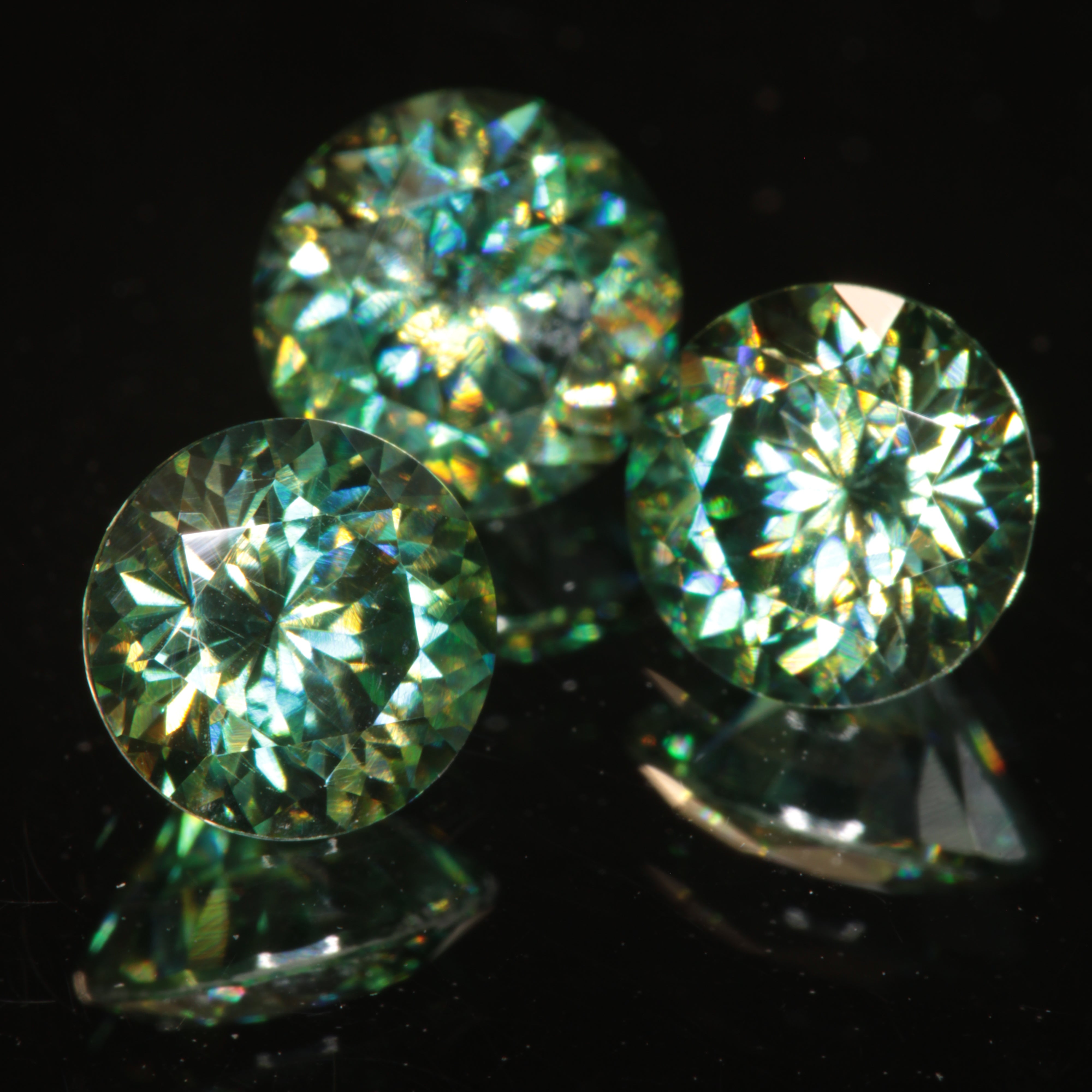 Green Moissanite Rounds on a black background showing dichroic colors