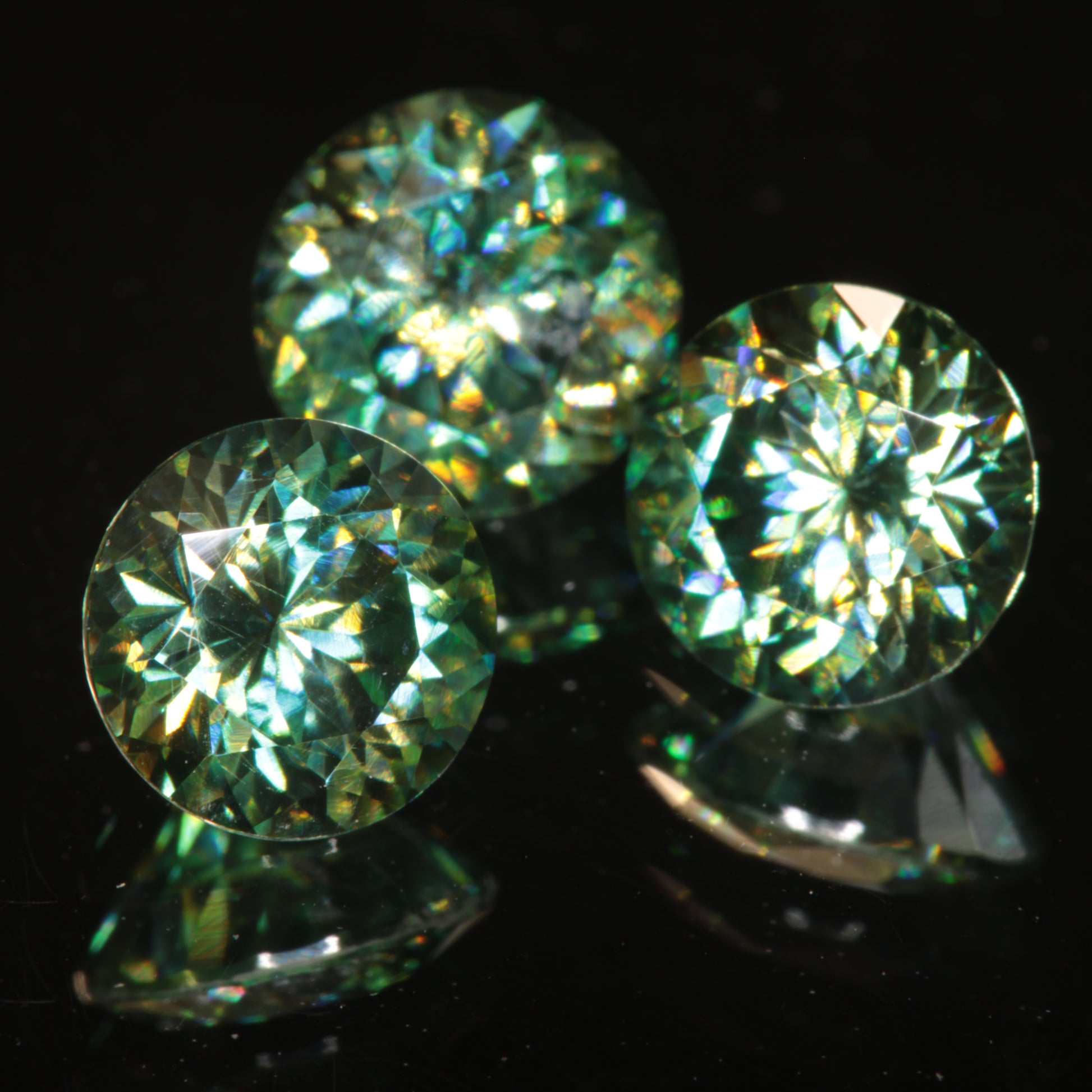 Green Moissanite Rounds on a black background showing dichroic colors