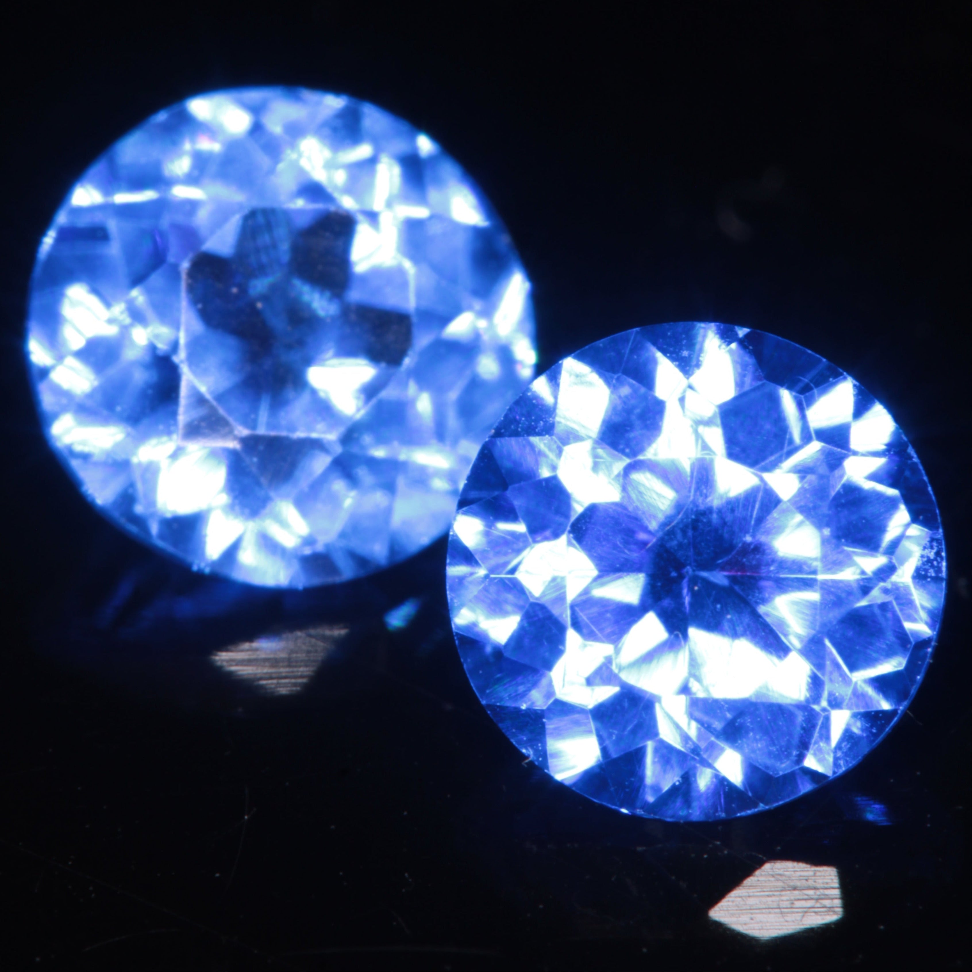 Two Faceted 5 mm Round Djeva Blue Spinel Gemstones, on a black background.
