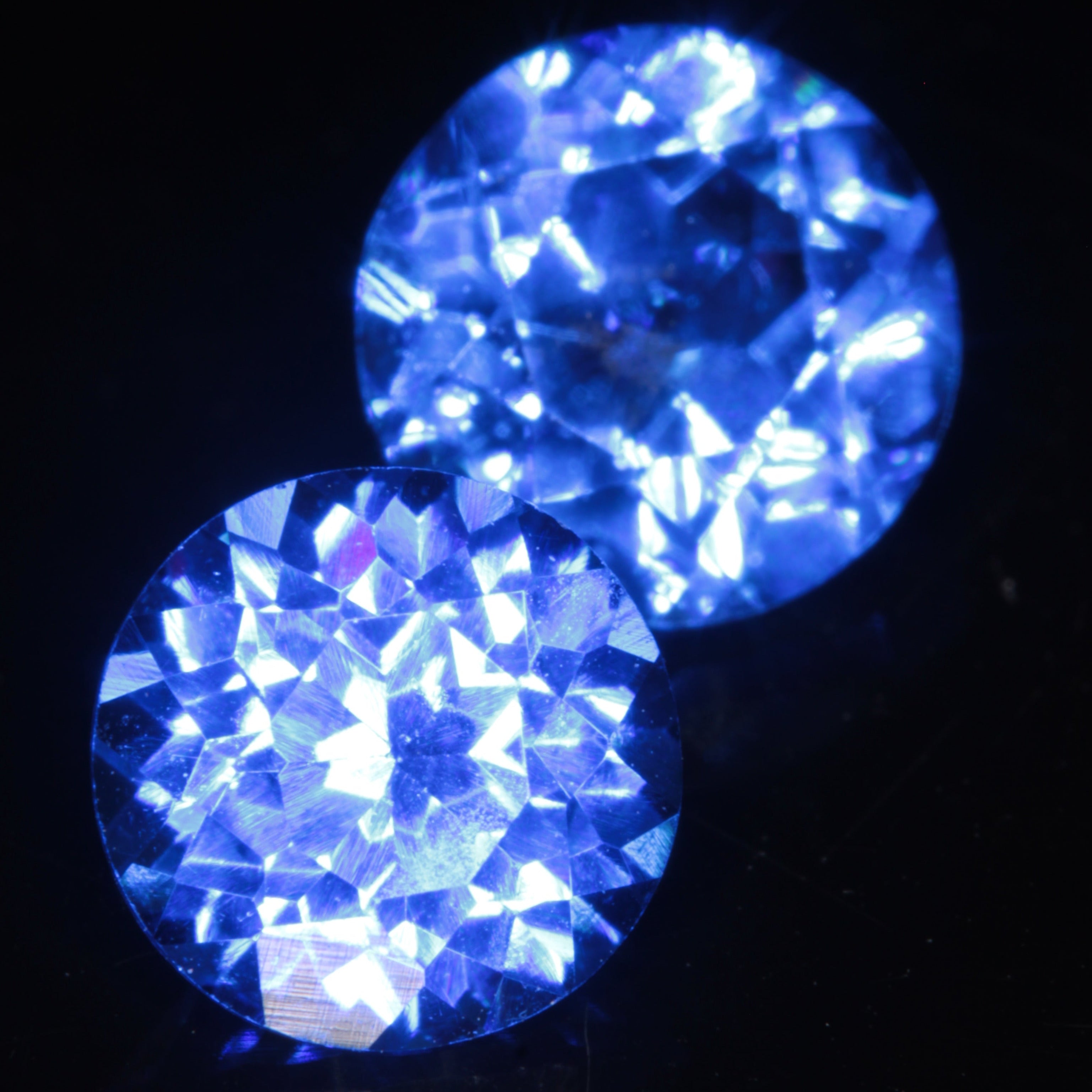 Two Faceted Round Djeva Blue Spinel Gemstones, 6 mm in diameter on a black background.