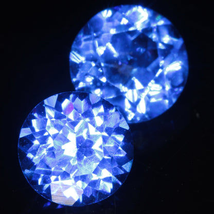 Two Faceted Round Djeva Blue Spinel Gemstones, 6 mm in diameter on a black background.