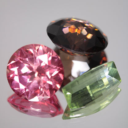 Three Faceted Soviet Fancy Sapphire Gems, Pink, Brown, and Green Faceted Sapphires on a Gray Background