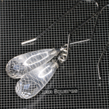 Clear faceted teardrop-shaped fluorite earrings with sterling silver fishhook ear wires, displayed on a black grid mat labeled '1mm Squares'.