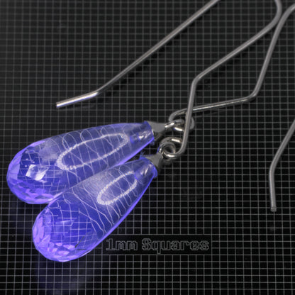 Clear faceted teardrop-shaped glowing blue fluorite earrings with sterling silver fishhook ear wires, displayed on a black grid mat labeled '1mm Squares'.