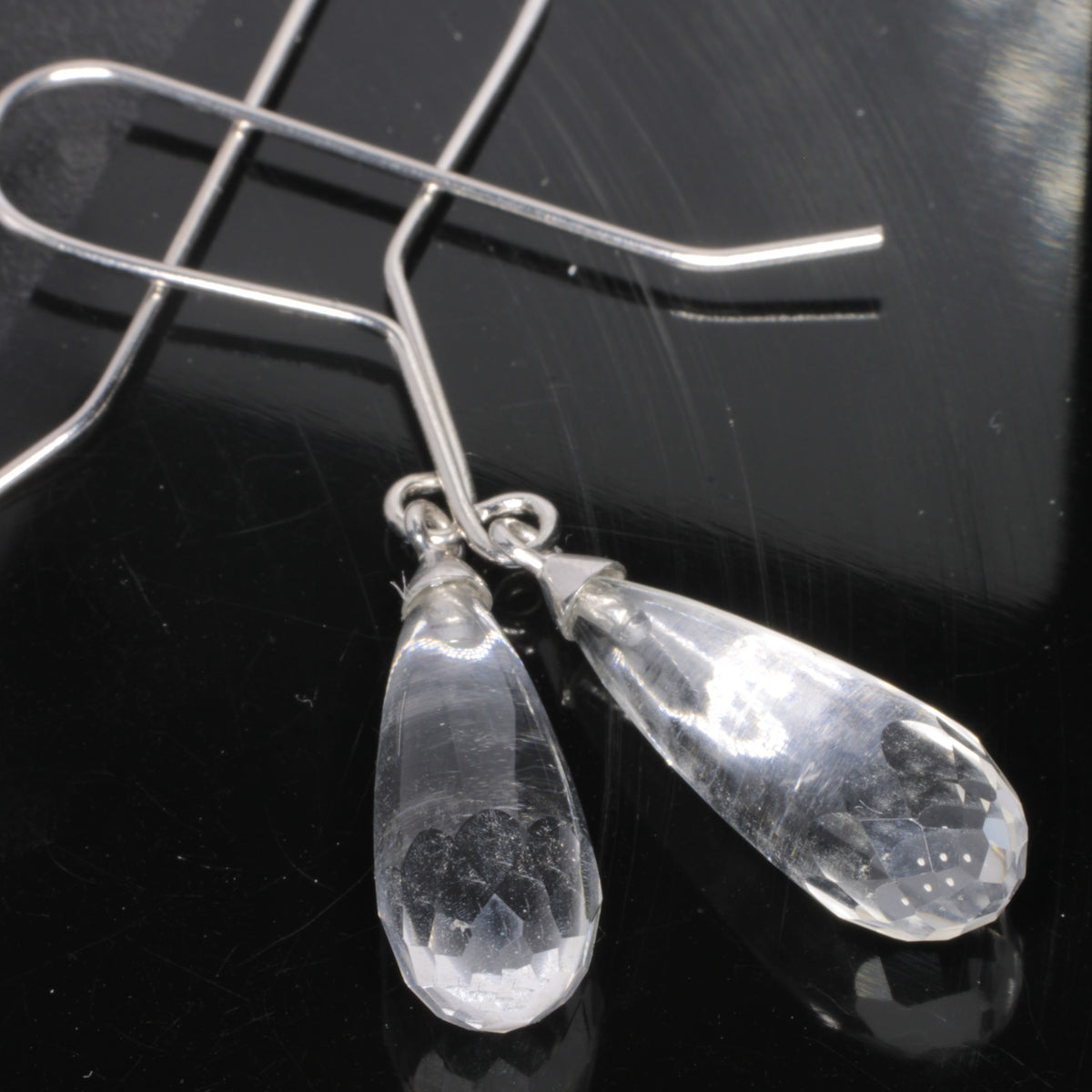 Faceted clear teardrop fluorite dangle earrings with silver wire hooks, displayed on a glossy black reflective surface.