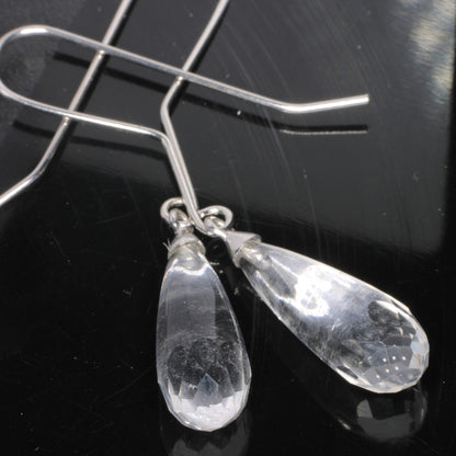 Faceted clear teardrop fluorite dangle earrings with silver wire hooks, displayed on a glossy black reflective surface.