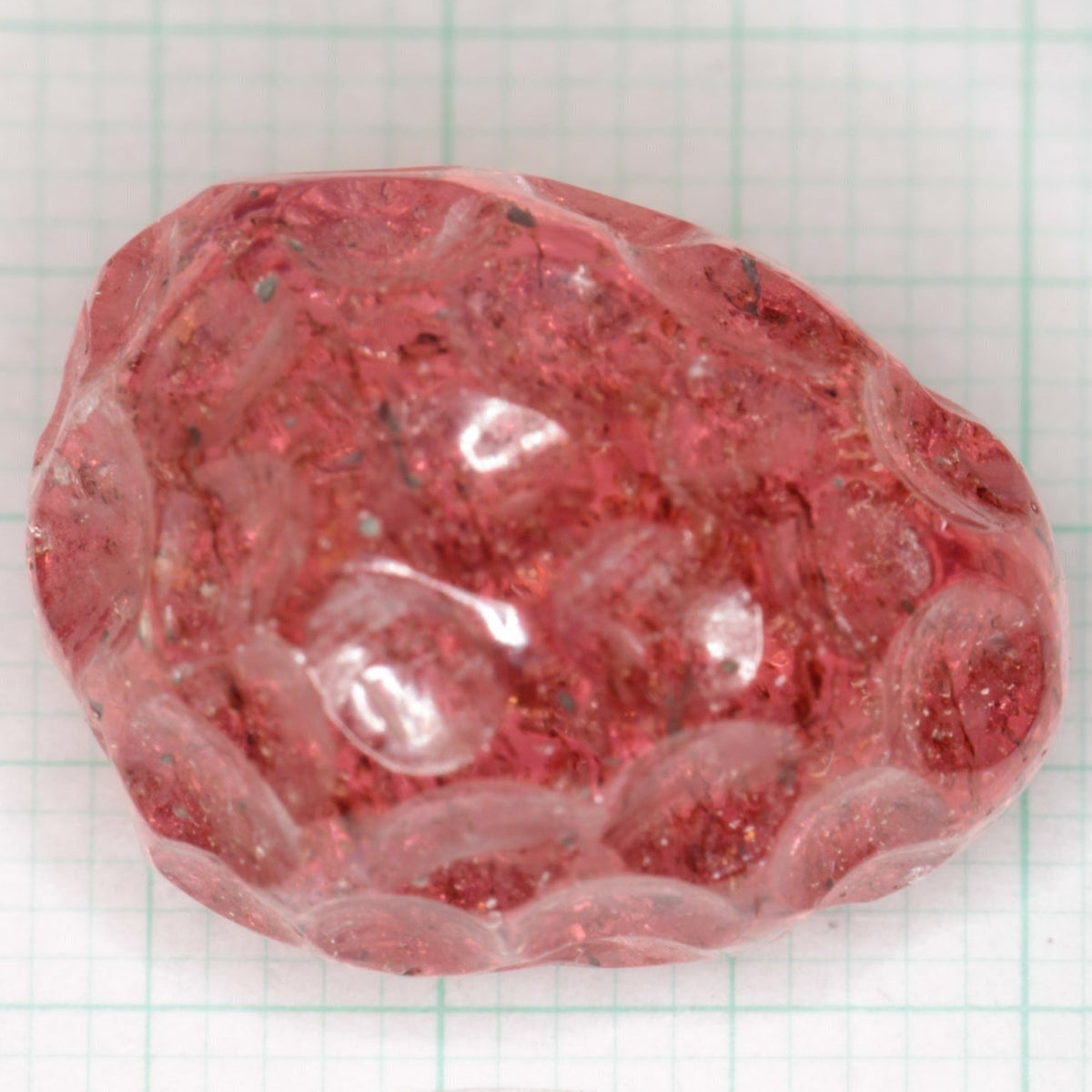 A carved laser sapphire resembling a strawberry with visible internal structure and bubbles, displayed against a dark background.