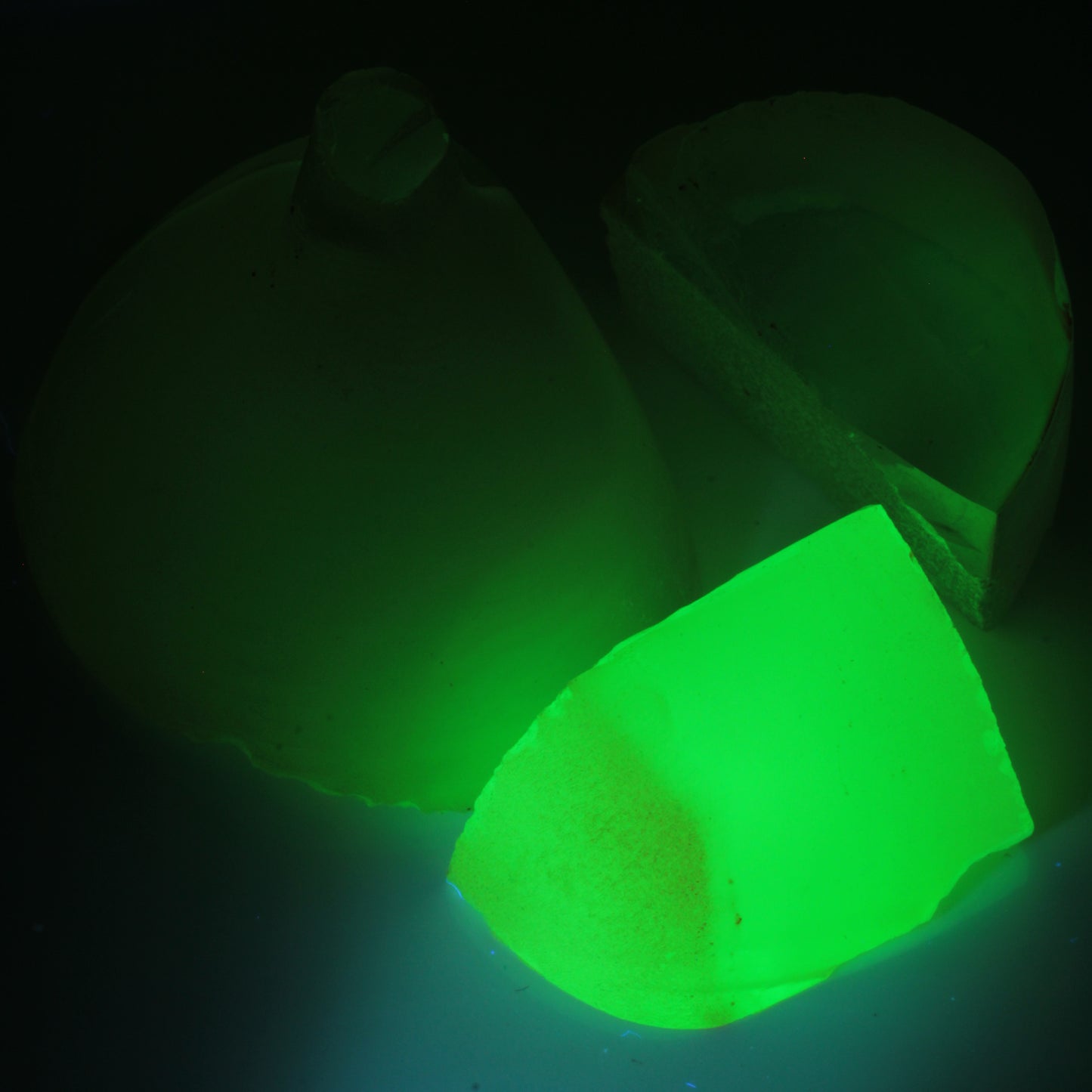 Three pieces of flame fusion green spinel under 365nm UV showing the green glow