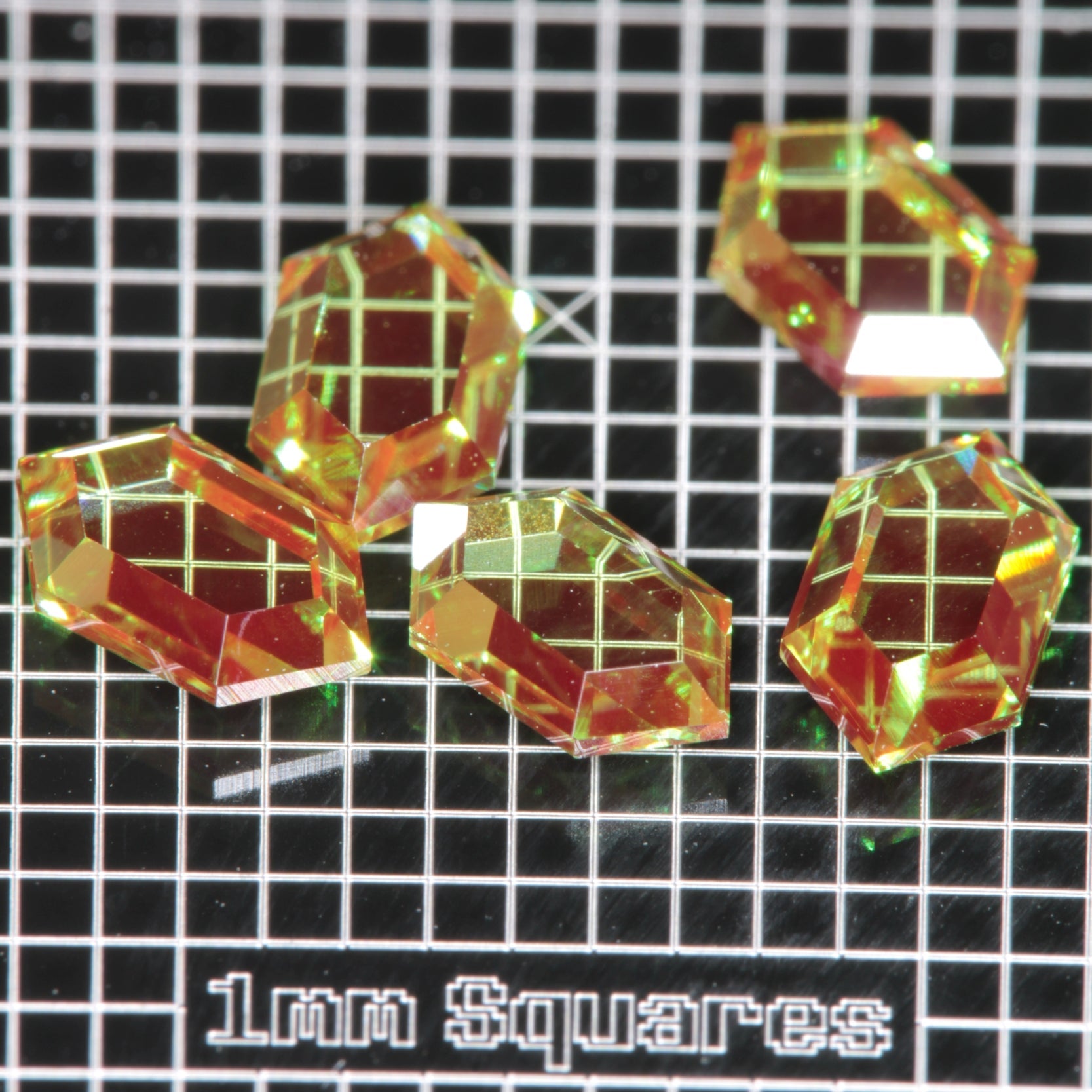 RetroHex faceted Christmas Garnets on a 1 mm grid for scale, Red and Green Cr+3:YAG gemstones