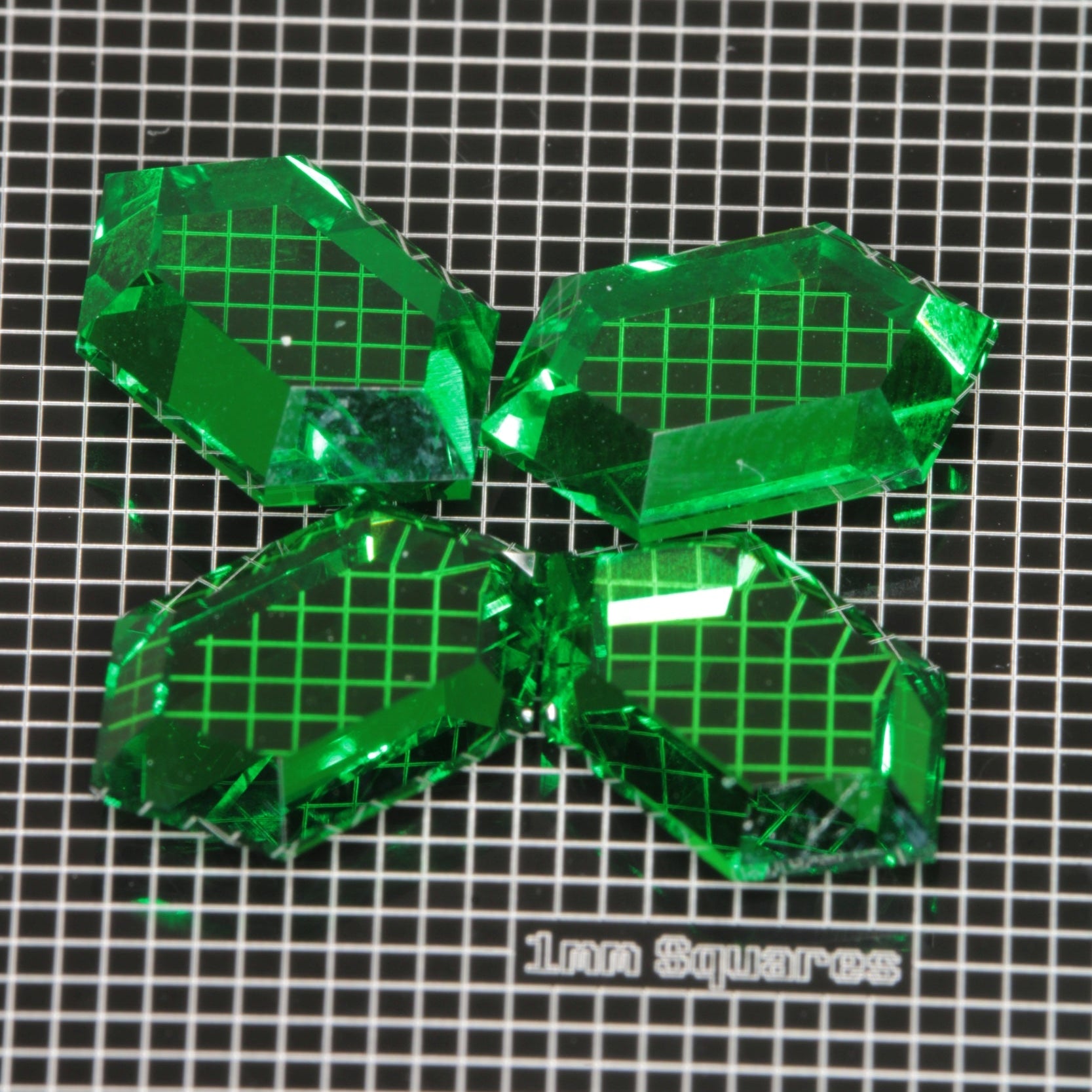 Green Retrohex faceted garnets on a 1 mm scale background