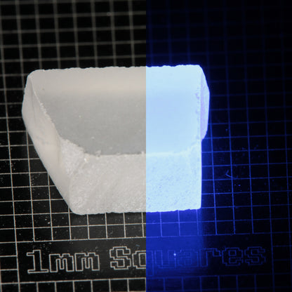 Block of LSO Gem Rough on a dark background, split between normal light (left) and UV (right) to show blue fluorescent glow.