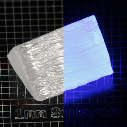 Wedge of LSO Gem Rough on a dark background, split between normal light (left) and UV (right) to show blue fluorescent glow.