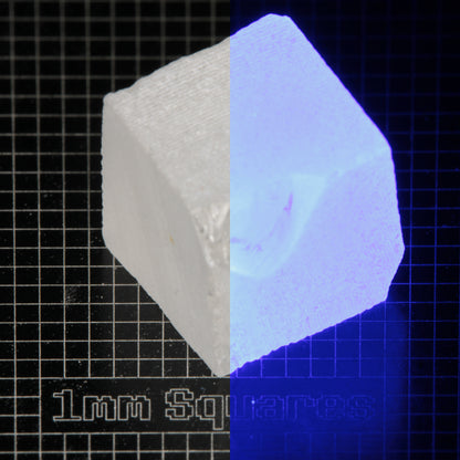 Block of LSO Gem Rough on a dark background, split between normal light (left) and UV (right) to show blue fluorescent glow.
