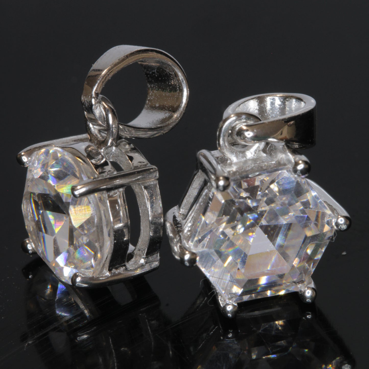 Two faceted TGG pendants set in sterling silver on a black background, showing their strong green fluorescene under UV