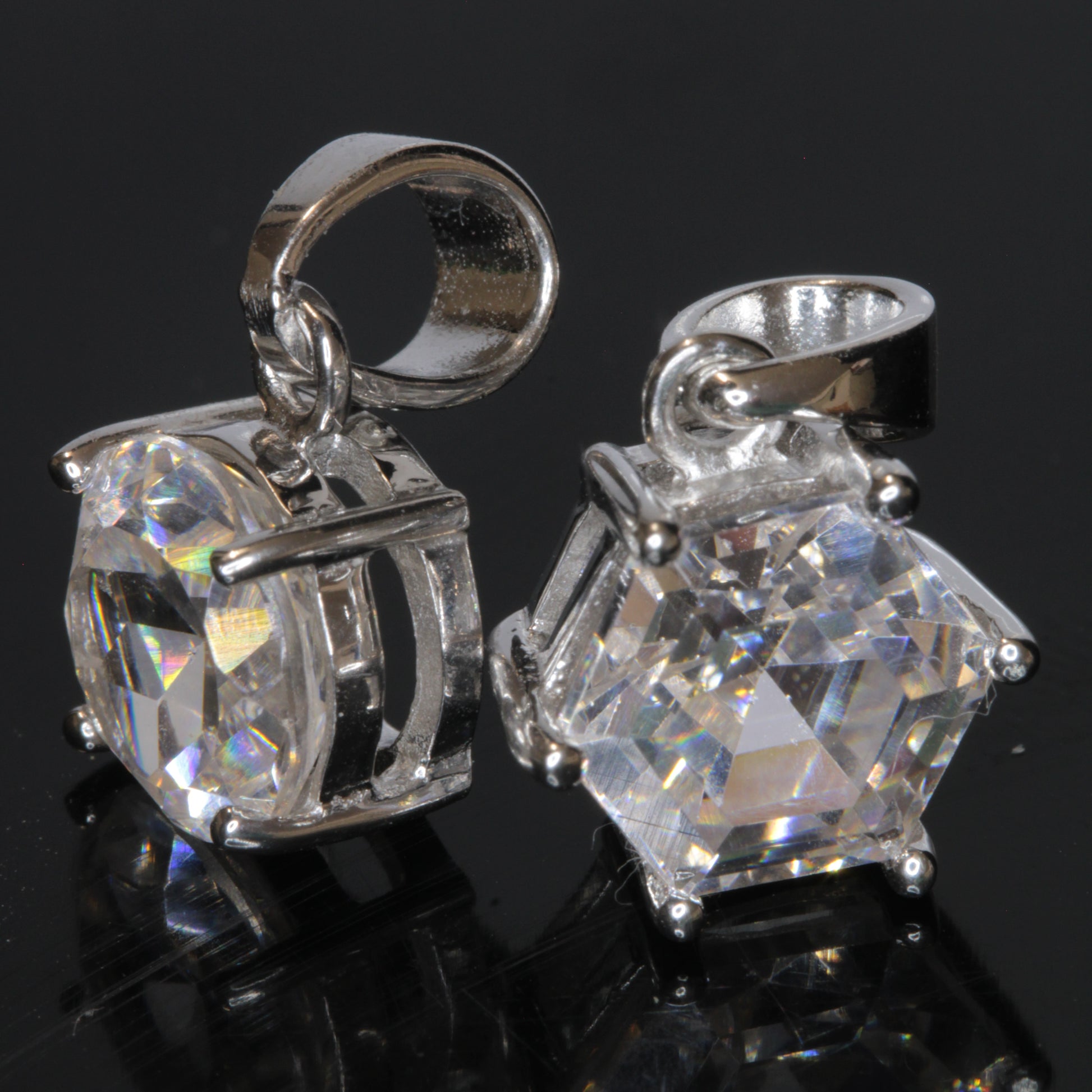 Two faceted TGG pendants set in sterling silver on a black background, showing their strong green fluorescene under UV