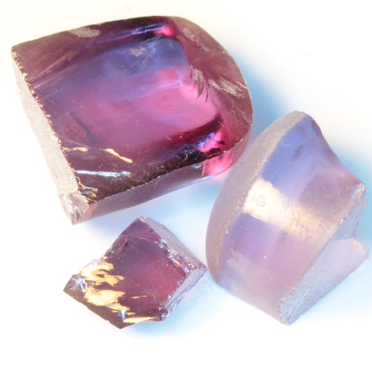 Three pieces of color change flame fusion sapphire rough under mixed lighting showing color from blue to red purples