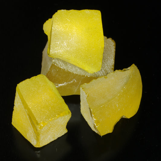 Four pieces of golden yellow Ce/Nd YAG gem rough on a black background