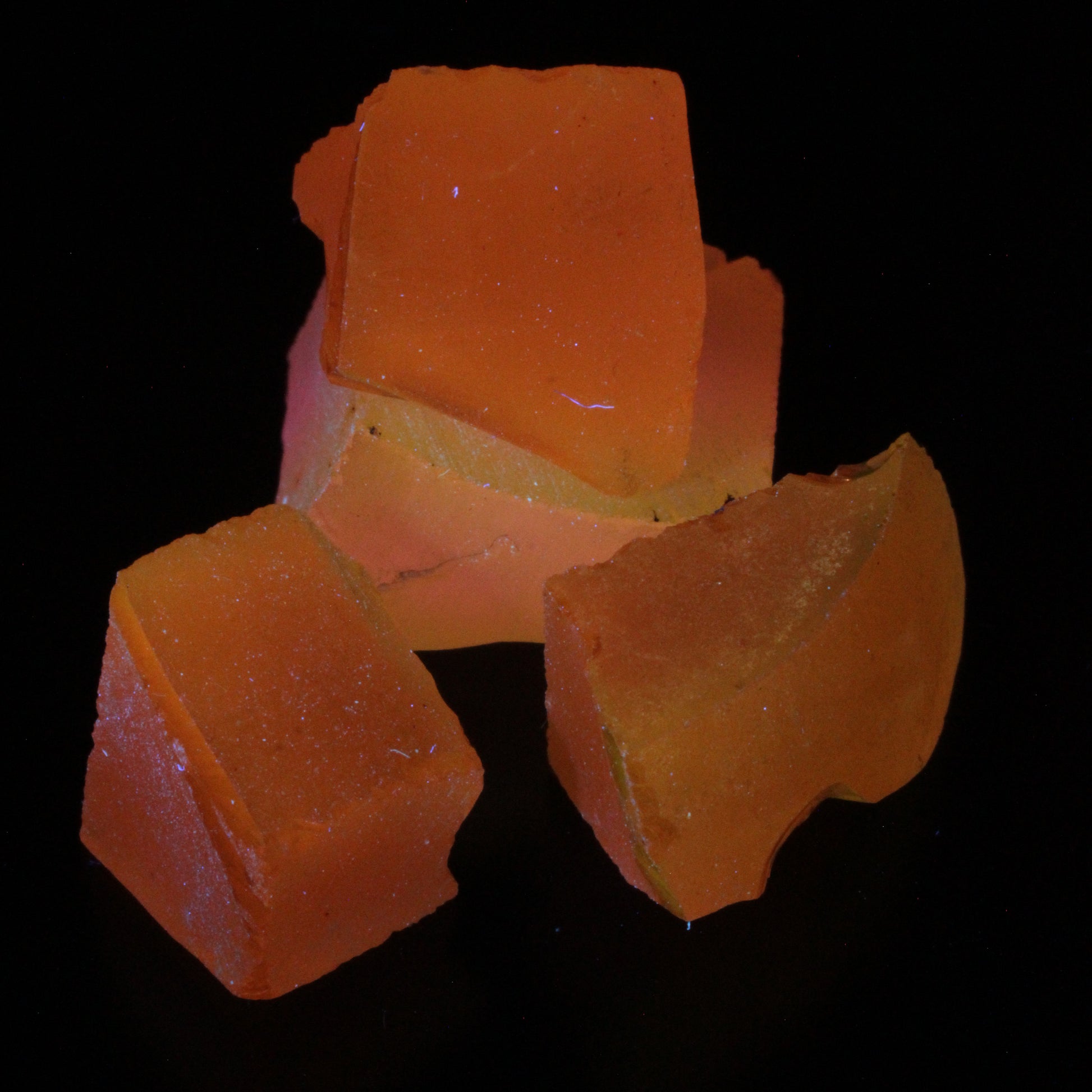 Four pieces of Ce/Nd YAG gem rough glowing pink and yellow under UV on a black background